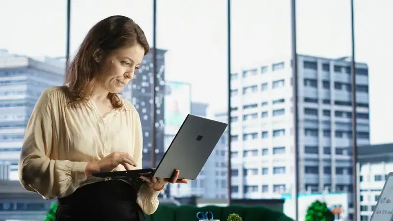 Administradora revisa un reporte en su laptop junto a una ventana con vista a edificios