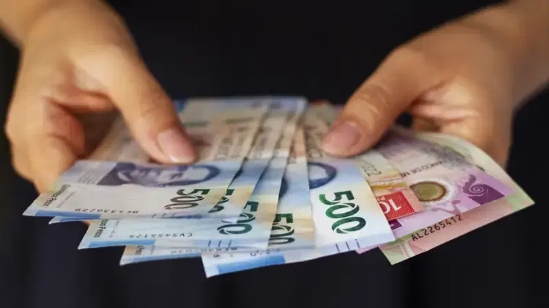 Manos sostienen billetes de pesos mexicanos, como referencia de las comisiones de cobro de cuotas en un condominio