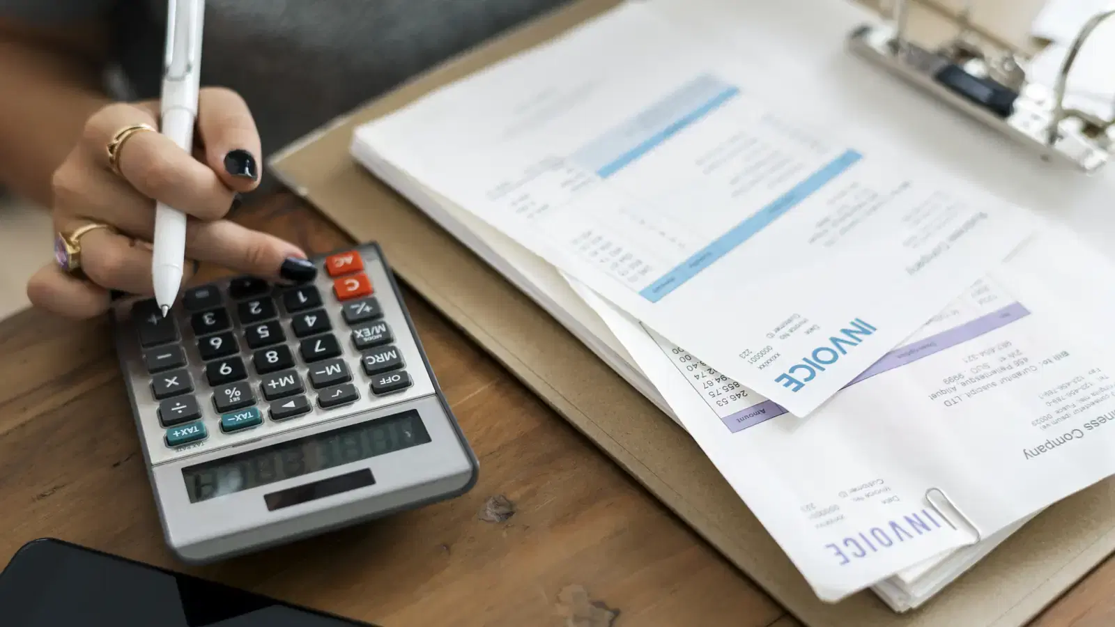 Manos revisan recibos con calculadora y pluma sobre un escritorio