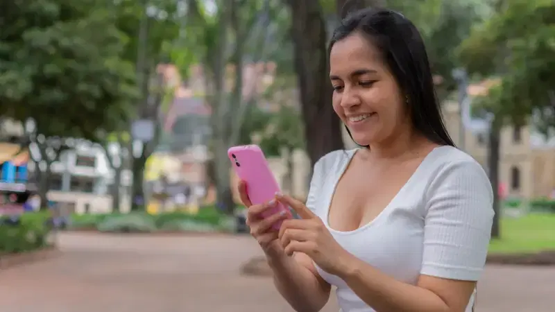 Mujer sonriente usa su celular en un parque