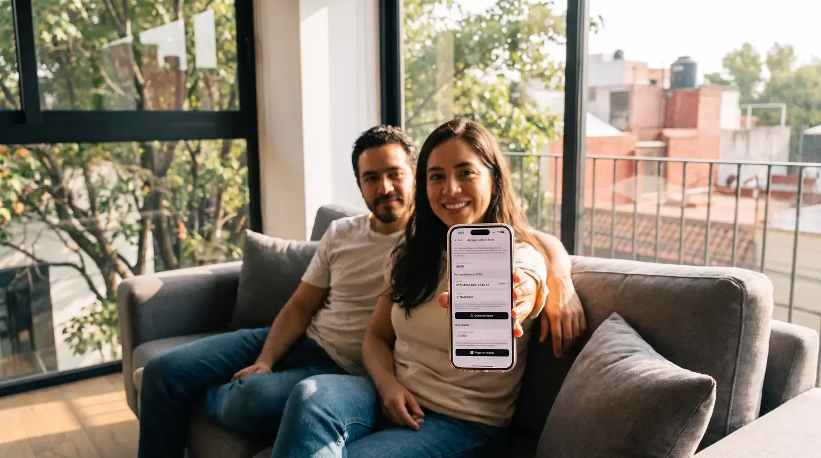 Pareja en su sala muestra en el celular el pago de la cuota de mantenimiento
